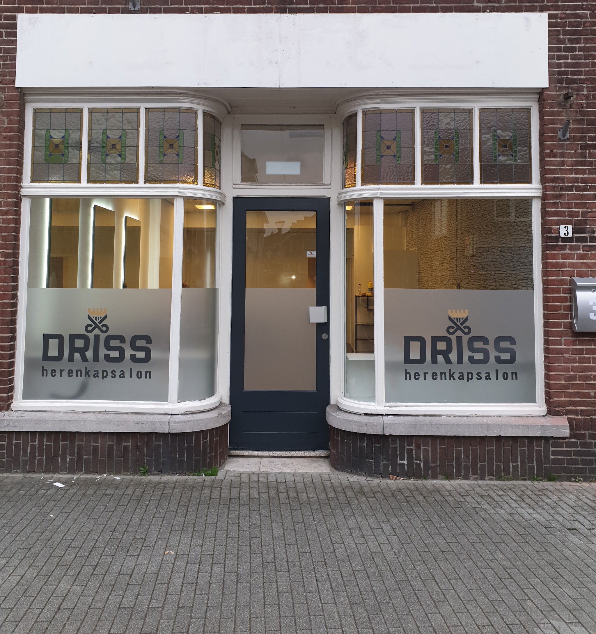De gevel van DRISS Herenkapsalon overdag, met glas in lood boven de etalageramen